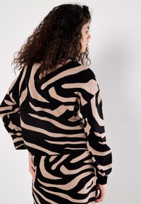Knit pullover in black and beige animal print with a relaxed fit, wide sleeves, and ribbed hem. Textured surface enhances visual interest.