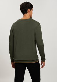 Zielony sweter z długim rękawem, okrągłym dekoltem i ściągaczami przy nadgarstkach. Tylna część ma płaską teksturę oraz kontrastowy brzeg w talii.