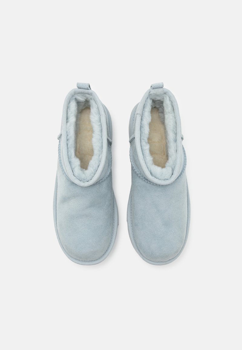 Bottes slip-on en suède bleu clair avec une doublure en fausse fourrure crème douce, bout arrondi et accents cousus autour de l'ouverture.