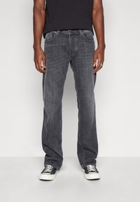 Jeans de mezclilla gris oscuro con corte recto, diseño de cinco bolsillos y detalles de costura visibles. Llevados con zapatillas negras.