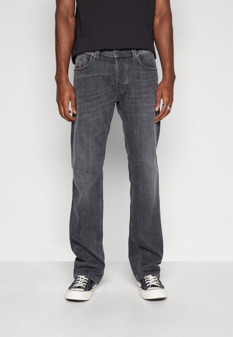 Jeans de mezclilla gris oscuro con corte recto, diseño de cinco bolsillos y detalles de costura visibles. Llevados con zapatillas negras.