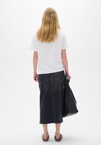 White short-sleeve t-shirt, dark denim mid-length skirt with back pockets, black shoulder bag, and beige slide sandals. Plain background.