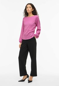 Fuchsia teksturert langermet topp med båthals, rysjekant nederst, kombinert med svarte skreddersydde bukser og svarte spisse hæler.