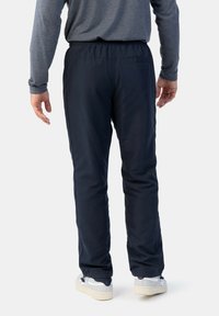 Marineblaue Sporthosen mit elastischem Bund, glatter Textur und schmal zulaufenden Beinen, die einen dezenten Glanz und Reißverschlüsse an den Säumen aufweisen.