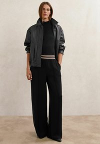 Must nahast jakk kõrge kraega, millele on lisatud must kootud särk ja laia säärega mustad püksid triibulise vööjoonega. Sile tekstuur.