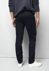 Chinos en coton bleu marine à coupe slim, dotés de poches arrière et d'un patch en cuir marron sur la taille, associés à des baskets blanches.