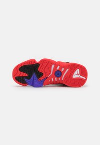 Semelle d'une chaussure de sport aux couleurs rouge, noire, violette et blanche, avec des motifs texturés antidérapants et un logo de la marque au niveau du talon.