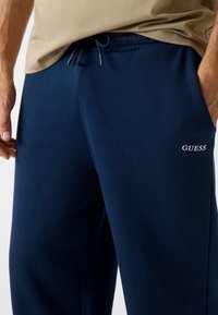 Marineblaue Jogginghose aus weichem Stoff mit elastischem Bund und Kordelzug. Verfügt über das weiße "GUESS"-Logo auf dem linken Oberschenkel.