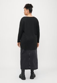 Schwarzes Langarmoberteil mit weit ausgeschnittenem Kragen, kombiniert mit einem dunkelgrauen Jeansrock; verfügt über eine gerade Passform und schwarze Stiefel bis zur Knöchelhöhe.