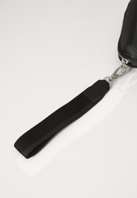 Bolsita negra con cremallera, con una superficie texturizada y una correa de tela para la muñeca que incluye un clip de metal plateado y costuras reforzadas en la correa.