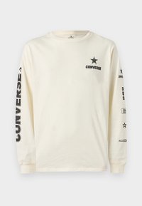 Κρεμ μακρυμάνικη μπλούζα με μαύρο λογότυπο αστεριού Converse και κείμενο στο στήθος, καθώς και εκτυπωμένη σήμανση κάθετα και οριζόντια και στα δύο μανίκια.