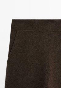 Pantalons tricotés marron foncé avec une texture lisse, une taille élastique et des poches latérales, avec une coupe droite conçue pour le confort.