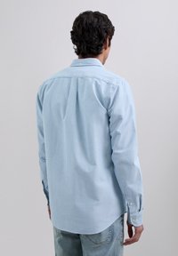 Chemise à manches longues à rayures bleu clair, en coton, col boutonné, ourlet légèrement incurvé et poignets boutonnés. Vue de dos affichée.