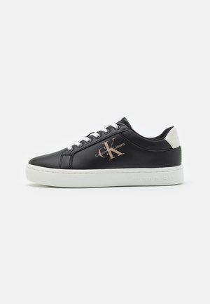 Black low-top sneaker with white sole and laces, featuring Calvin Klein Jeans logo on side and heel tab, against a plain white background.
