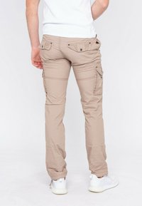 Pantalons cargo beiges en tissu léger, dotés de plusieurs poches, de détails cousus et d'une coupe fuselée aux chevilles. Portés avec des baskets blanches.