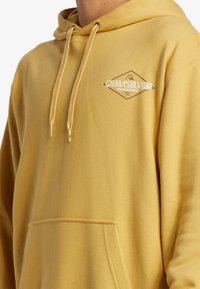 Yellow hoodie made from soft fabric with a drawstring, featuring a front pocket and a Quiksilver logo in white on the chest.