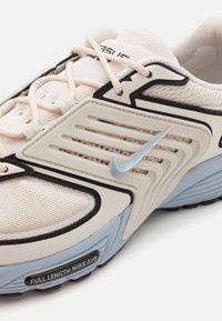 Bílá a světle modrá sportovní obuv s síťovaným svrškem, černými detaily a gumovou podrážkou. Vlastnosti zahrnují šněrování a viditelné logo Nike.