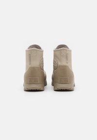 Beżowe wodoodporne botki za kostkę z teksturowaną gumową podeszwą, wyposażone w zaokrąglony nosek, wyściełany kołnierz oraz wytłoczone logo na pięcie.