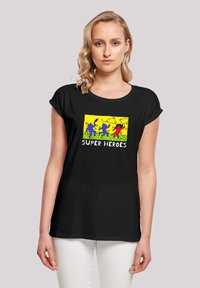 Black t-shirt with short rolled sleeves featuring a colorful graphic of four superheroes on a yellow background, text "SUPER HEROES" below.