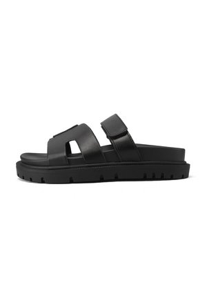 Sandali in pelle nera con una larga fascia caratterizzata da un design a intagli e chiusura regolabile, montati su una suola in gomma testurizzata.