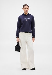 Námořnická mikina s kapucí s nápisem "GANT1949", krémové široké kalhoty a černá kabelka z umělé kožešiny. Obuv je černá s kulatou špičkou.