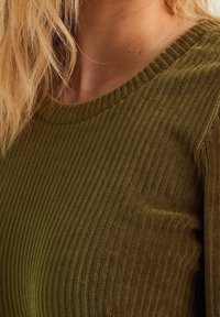 Top a costine in verde oliva con scollo rotondo e tessuto testurizzato, caratterizzato da una struttura aderente e linee di tessuto visibili.