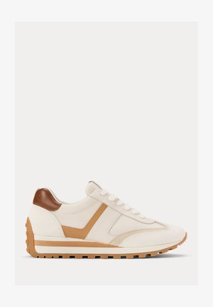 Beige en bruine lage sneaker met witte veters, een getextureerde zool en een bruine hielpatch, weergegeven in zijaanzicht op witte achtergrond.