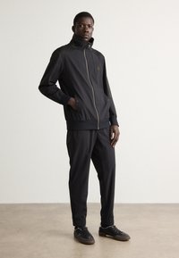 Black athletic tracksuit in lightweight fabric, featuring a zippered jacket with stand collar, tapered pants with cuffs, and sneakers.