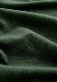 Tissu doux vert foncé avec un motif tricoté fin et texturé montrant des plis et des ombres délicats.