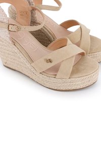 Sandalias de cuña beige con diseño de tiras cruzadas, hechas de suave ante y con detalles de cuerda trenzada en el talón, presentando un pequeño acento metálico con logo.