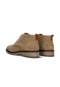 Bottines en suède beige à bout rond et semelle en caoutchouc marron. Elles disposent d'une petite languette en cuir au niveau du talon et d'accents cousus.