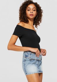 Top negru, cu umerii la vedere, asociat cu o fustă mini din denim de nuanță deschisă, având o curea lată texturată și un tiv desfăcut.