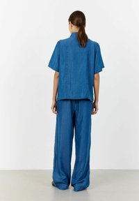 Denimowy zestaw składający się z luźnej, krótkiego rękawa bluzki oraz spodni z szerokimi nogawkami w średnim odcieniu niebieskiego, prezentujący gładką teksturę.
