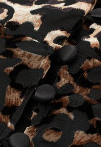 Leopardprint stof met zwarte, bruine en crèmekleurige texturen, verfraaid met zwarte knopen als opvallende accenten. Patroonontwerp met een zachte textuur.