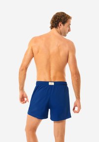 Pantaloni da bagno blu con una cintura elastica, dotati di un'etichetta sul retro. Il tessuto sembra leggero e liscio al tatto.