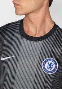 Grijs en zwart gestreept voetbalshirt met een ronde halslijn, met een wit Nike-logo en een cirkelvormig Chelsea FC-embleem op de linker borst.