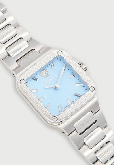 Montre-bracelet carrée en métal argenté avec cadran bleu, index et aiguilles argentés, logo Versace et motif clé grecque sur la lunette et le bracelet.