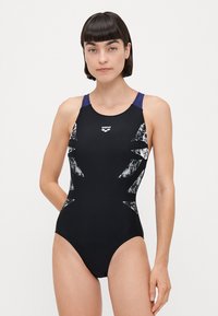 Svart badetøy med et hvitt abstrakt mønster på sidene, racerback-design og lilla aksenter på skulderstroppene.