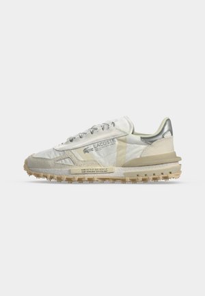 Basket Lacoste blanche et beige avec semelle texturée, détail talon argenté et logo sur le côté, présentée en profil sur un fond uni.