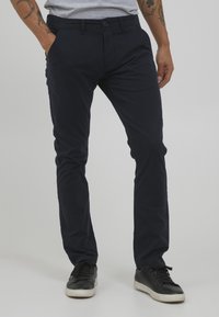 Pantaloni in cotone blu navy con vestibilità slim, dotati di tasche laterali e chiusura con un bottone. Indossati con sneakers nere.