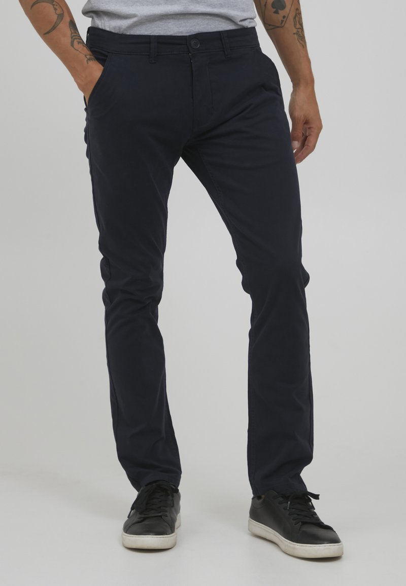 Pantaloni in cotone blu navy con vestibilità slim, dotati di tasche laterali e chiusura con un bottone. Indossati con sneakers nere.