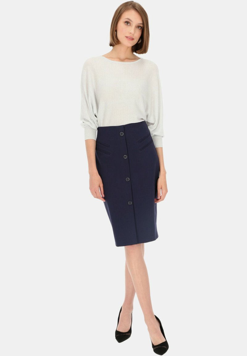 Granatowa spódnica ołówkowa z guzikami z przodu i teksturowanymi paskami, połączona z jasnoszarym topem z luźnymi rękawami. Czarne szpilki.