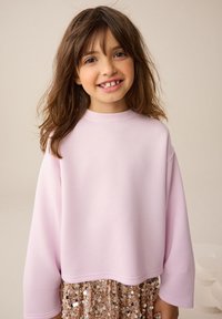 Light pink long-sleeve sweatshirt with a round neckline, featuring a loose fit. Paired with a sparkly sequined skirt in gold tones.
