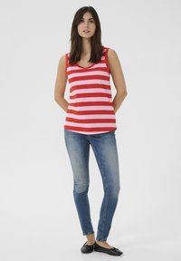 Débardeur rayé rouge et rose avec un col arrondi, assorti à un jean skinny bleu et des chaussures plates noires. Design simple et coupe décontractée.