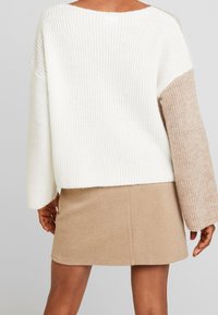 Sweat-shirt oversize en maille blanche texturée avec une manche en tricot beige. Associé à une jupe beige, avec une coupe décontractée et un design simple.