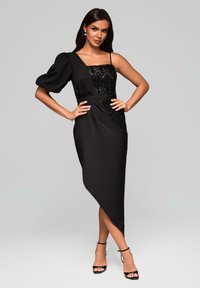 Schwarzes asymmetrisches Kleid mit einem Puffärmel, Pailletten-Bustier, seitlicher Drapierung und hohem Schlitz, kombiniert mit schwarzen Riemchenhebeln.