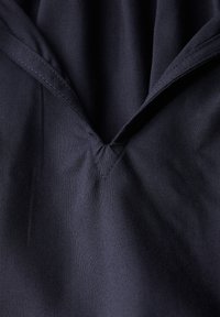 Tessuto blu navy con una finitura testurizzata, caratterizzato da un scollo a V e cuciture ordinate, che enfatizzano un design liscio e strutturato.