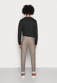 Černá mikina s kulatým výstřihem, doplněná o hnědé kostkované kalhoty. Bílé ponožky a hnědé tenisky dotvářejí outfit.