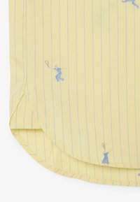 Angolo di tessuto giallo con sottili strisce verticali blu e piccoli motivi di tennisti blu che tengono racchette sparsi sul materiale.