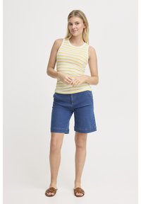 Top sin mangas a rayas amarillas y blancas combinado con pantalones cortos de mezclilla azul Bermuda. Los pantalones cortos tienen un dobladillo doblado y bolsillos laterales. Sandalias marrones tipo playero.